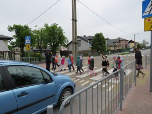 dzieci przechodzące przez przejście dla pieszych z podniesioną rękom i na środku przejścia stojąca policjantka