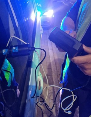 policjant za pomocą specjalistycznego urządzenia bada poziom przepuszczalności światła w samochodzie