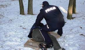 Umundurowany policjant pochyla się nad człowiekiem leżącym na śniegu