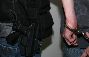 dłonie w kajdankach i broń przy pasie policjanta
