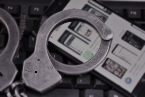 Fotografia czarno biała: klawiatura komputerowa na której widzimy kajdanki policyjne i telefon komórkowy