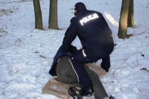 Fotografia kolorowa: na śniegu lezący bezdomny a przy nim pomagający mu policjant.
