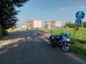 Fotografia kolorowa: droga, przy nieczytelnym przejściu dla pieszych i przekrzywionym znaku drogowym stoi motocykl policyjny - lustracje dróg.