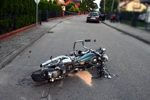 uszkodzony motocykl leżący na jezdni, w tle samochód osobowy