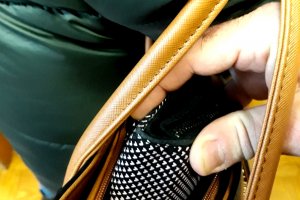 zdjęcie ilustrujące kradzież kieszonkową, ręka mężczyzny sięgającego po portfel, znajdujący się w torebce damskiej.