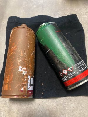 Dwie puszki farby w sprayu. Puszka po lewej jest ubrudzona brązową farbą, natomiast po prawej jest pokryta zieloną farbą