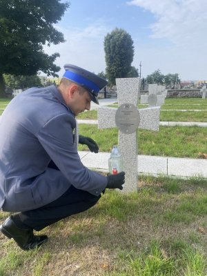 Policjant stawiający znicz na ziemi na cmentarzu wojennym w Trojanowie