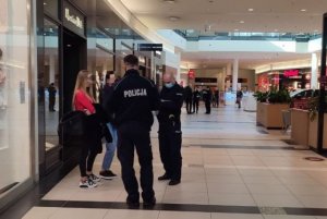 Dwóch umundurowanych policjantów kontroluje dwie kobiety w centrum handlowym