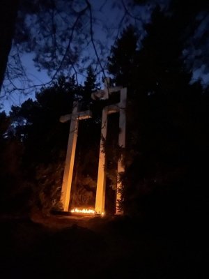 Trzy krzyże na cmentarzu w Palmirach. Na ziemi stoją zapalone znicze