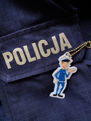 Fragment granatowego munduru z kieszenią na której jest napis Policja. Obok leży odblask z motywem policjanta
