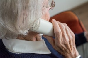 Starsza kobieta trzyma słuchawkę telefonu stacjonarnego przy uchu