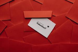 Czerwone koperty, a na środku biała kartka z napisem will you be my valentine?