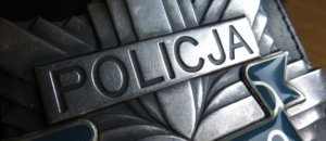 Zdjęcie przedstawia część metalowej odznaki policyjnej w kształcie gwiazdy. W górnej części napis Policja