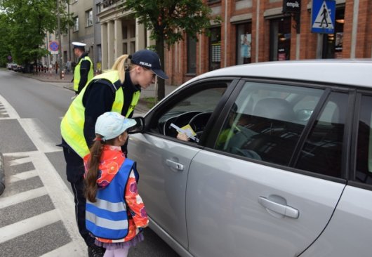 Policjantka z dziewczynką rozmawia z kierowcą samochodu.
