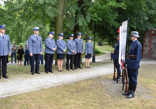 Posterunek grupy rekonstrukcji historycznej III Okręgu Policji Państwowej Komisariat w Radomiu przy tablicy pamiątkowej, po lewo policjanci zebrani na odsłonięciu tablicy.
