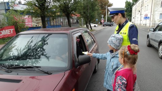 Dzieci wręczają naklejki dla kierowców wraz z policjantką