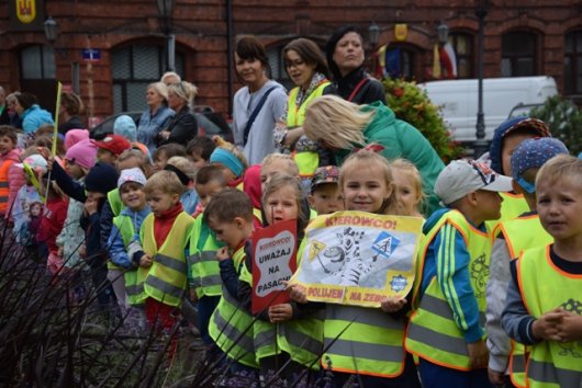 Dzieci biorące udział w happeningu &quot;Kierowco! Nie polujemy na zebrach&quot;. Dzieci ubrane w kamizelki odblaskowe trzymają plakaty z hasłem działań.