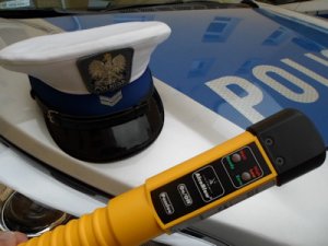 na pokrywanie od silnika samochodu z napisem policja znajduje się biała czapka policjanta ruchu drogowego i urządzenie do pomiaru alkoholu w organizmie człowieka