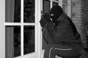 zdjęcie czarno - białe na którym widoczny jest człowiek z kominiarką na twarzy kucający przy oknie